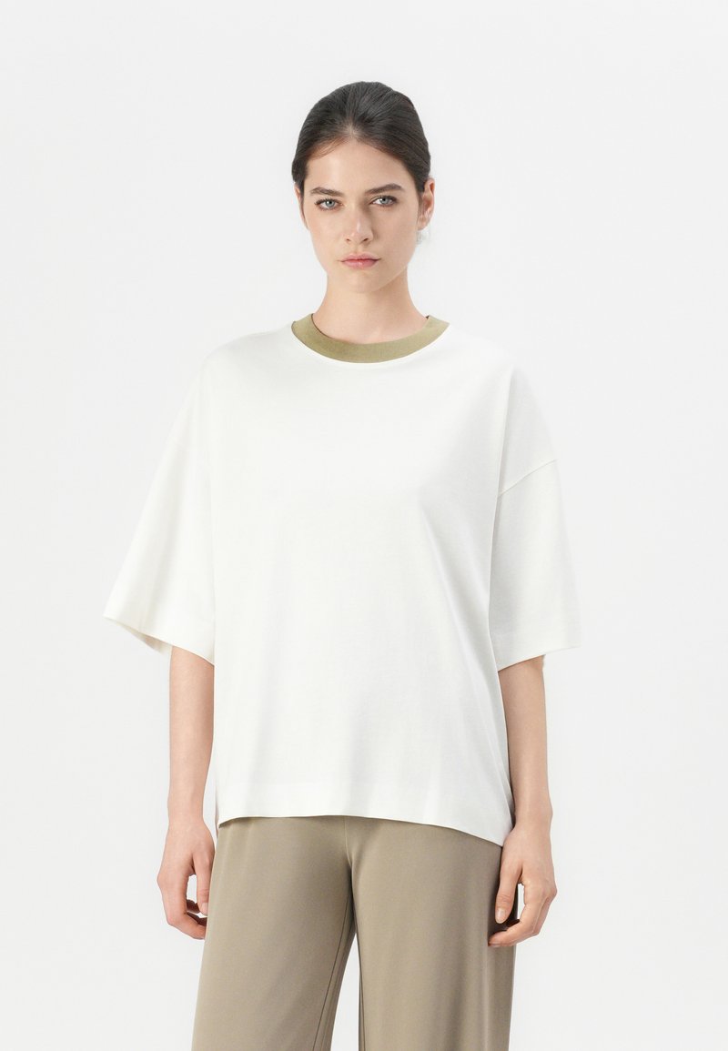 Witte oversized t-shirt met korte mouwen en een olijfgroen ronde hals. Zachte stof, losvallende pasvorm en recht afgebroken ontwerp.