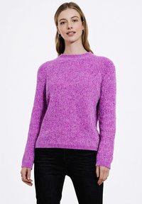 Fioletowy sweter z ribstopu, z długimi rękawami i okrągłym dekoltem, o teksturowanym wykończeniu. Zestawiony z czarnymi dżinsami.