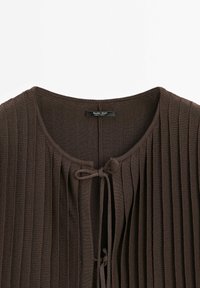 Brown ribbed knit cardigan with a round neckline, featuring a front tie closure and horizontal pleats along the fabric. Brand label visible.