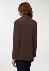 Brązowa marynarka z korduroyu z wyciętym kołnierzem, trzema guzikami na rękawach i dopasowanym krojem. Gładka tekstura i wyraźny kształt.