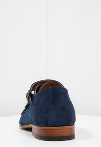 Chaussure en daim bleu marine à finition lisse, bout arrondi et talon en bois. Dispose d'une boucle décorative sur le côté.