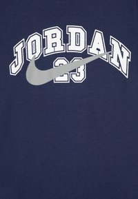 Mornarska majica s belim napisom "JORDAN 23" in sivo Nike znak. Izdelana iz mehke tkanine s klasičnim krojem okoli vratu.