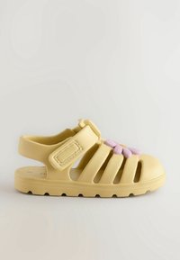Sandale jaune à bout fermé avec bride ajustable et décoration fleur violette sur le dessus, conçue pour enfants.