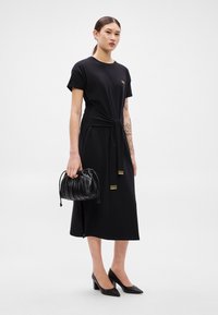 Μαύρο φόρεμα με κοντά μανίκια και στρογγυλή λεπτομέρεια στο μπροστινό μέρος, με χρυσαφένιες μεταλλικές λεπτομέρειες. Συνοδεύεται από πλεκτή μαύρη τσάντα και μυτερές ψηλοτάκουνες γόβες.