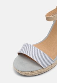 Sandale compensée avec bout en daim gris, bride avant en tissu rayé, bride de cheville beige, et semelle enveloppée de jute.
