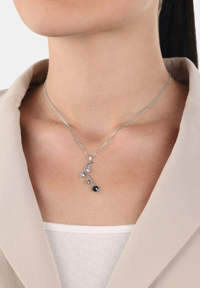 Silvrig halsband med ett hänge som har en blommig design, flera ädelstenar i nyanser av blått och klart, på en delikat kedja.