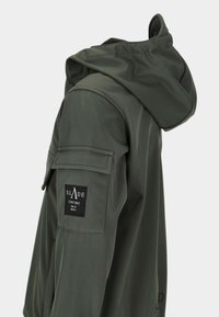 Ciemnozielona kurtka z kapturem z klapką kieszeni na górnym rękawie, z czarną naszywką marki Slade Couture.