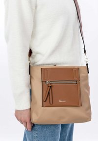 Borsa a tracolla marrone e beige in pelle sintetica; presenta una tasca con zip anteriore, cinturino regolabile, logo e linee pulite.