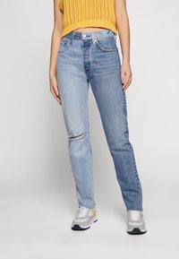 Lichtblauwe denim jeans met een relaxte pasvorm, met een gescheurde knie detail, klassiek vijf-pocket ontwerp en een hoge taille. Gedragen met sneakers.