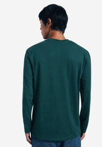 Grün langärmliges Shirt mit rundem Halsausschnitt, aus weichem Stoff gefertigt, mit lockerer Passform und schlichtem Design.