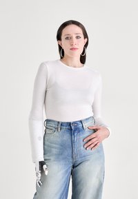 Hvit langermet topp laget av gjennomsiktig stoff, kombinert med høy midje blå denimjeans; har en robotarm på venstre arm.