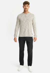 Maglia Henley a maniche lunghe grigio chiaro con motivo strutturato, abbottonatura a tre bottoni, abbinata a jeans neri e scarpe da ginnastica bianche.