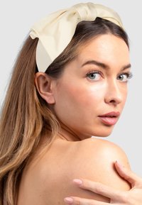 Light beige fabric headband with a large bow detail. Smooth texture, wider band, and gathered fabric at the bow tie.
