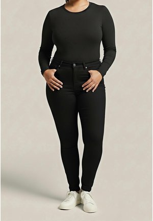 Woman standing wearing a fitted black long-sleeve top, black high-waisted skinny pants, and white sneakers against a neutral background.