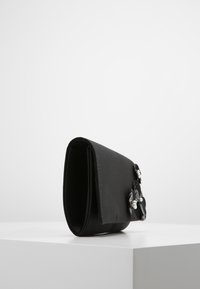 Bolso de mano de tela negra con una textura suave, adornado con elementos florales y acentos de perlas, estructurado en forma rectangular.
