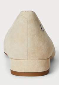 Beidzē ar zemu, brūnu gumijas papēdi, beidža zamša slip-on kurpe. Iezīmēta ar šūtu šuvi un nelielu sudraba aksesuāru sānos.