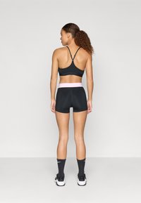 Čierny športový top s nastaviteľnými ramienkami a zodpovedajúce vysoké šortky s ružovým pásom, doplnené čiernymi členkovými ponožkami a teniskami.