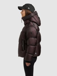 Puffy dark purple jacket with a high collar, zippered pockets, and a matte texture. Paired with a black cap, shown from the side.