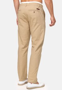 Beige linnedragter med løst fit, der har to baglommer med knapper og en elastisk talje. Parret med hvide slip-on sko.