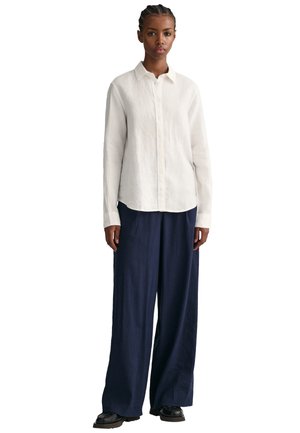 White linen button-up shirt paired with navy wide-leg pants and black shoes. The shirt features a collar and front placket.