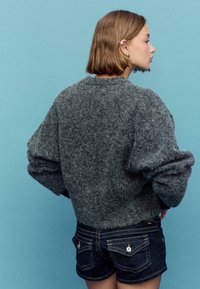 Sivi puhasti pulover z nizko ramena in širokimi rokavi, kombiniran z jeans kratkimi hlačami z zadnjimi žepi in gumbno dekoracijo.