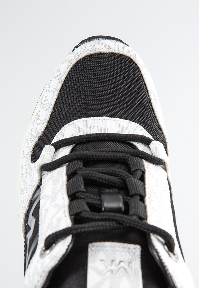 Baskets au design noir et blanc ; elles présentent un dessus texturé à motifs blancs, des sections en maille noire, des lacets noirs et des accents métalliques.