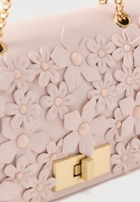 Bolso de mano de cuero rosa con aplicaciones florales en 3D y centros de color rosa pálido, con correas de cadena dorada y cierre rectangular dorado.