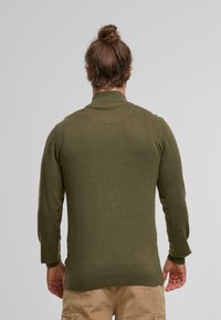 Olivengrüner Pullover mit hohem Kragen, langen Ärmeln und taillierter Passform. Glatte Textur mit gerippten Bündchen und Saumakzenten.