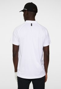 White short-sleeve polo shirt with a smooth texture, featuring a mesh panel on the side and a small black logo at the back collar.