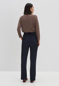 Bruine lange mouwen top gecombineerd met marineblauwe wijdvallende broek met een gladde textuur en twee achterzakken. Model is van achteren te zien.