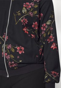 Veste bomber noire avec des motifs floraux roses et dorés. Dotée d'une fermeture éclair à l'avant et d'un ourlet et des poignets côtelés pour une coupe ajustée.