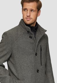 Grau texturierter Mantel mit hohem Kragen, schwarzen Akzenten und zwei Knöpfen. Verfügt über eine Reißverschlusstasche und auffällige Steppdetails.