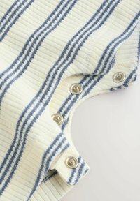 Trikotažni telesni kombinezon z bombažem v kremni barvi z mornarsko modrimi črtami, ki ima zapiranje s pritisnimi gumbi na rami. Rebrasta tekstura dodaja dodatne podrobnosti.