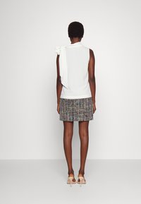 Haut blanc sans manches avec un détail de nœud sur le côté, associé à une mini-jupe texturée multicolore. Le mannequin porte des talons de couleur claire.