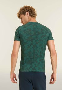 T-shirt à manches courtes camouflage vert en tissu doux. Doté d'un col rond et d'une coupe ajustée, avec des variations subtiles de tons de couleur.
