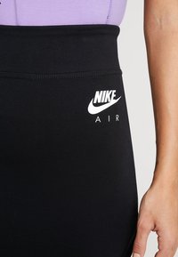 Svarta leggings med en åtsittande design, med en bred midja och en vit Nike Air-logotyp på sidan. Slätt, elastiskt material.