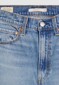 Vaqueros de mezclilla azul claro con diseño de campana, que presentan remaches de cobre, costuras naranjas y una etiqueta que indica la talla 27.