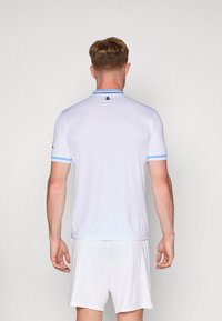 Polo sportivo bianco a maniche corte, con colletto e polsini azzurri chiari, caratterizzato da un piccolo logo sulla parte posteriore vicino al colletto.