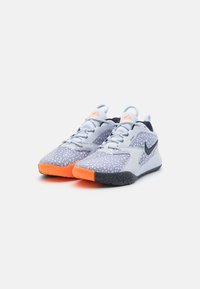 Lys grå sneakers med tekstureret mønster, orange detaljer på sålen, sort logo og snørebåndsdesign. Har en rund tå og polstret hæl.
