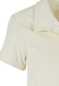 Chemise texturée couleur crème à manches courtes, présentant un col plié et des coutures visibles à l'épaule et à la manche.
