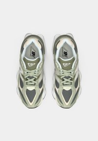 Baskets de sport vertes et beiges avec un dessus en maille et synthétique, au design élégant, avec un laçage prononcé et une semelle blanche arrondie.