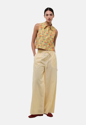 Top crop floral jaune avec des motifs rouges et verts ; pantalon large à rayures jaunes et blanches ; chaussures rouges ; tissu lisse ; coupe décontractée.