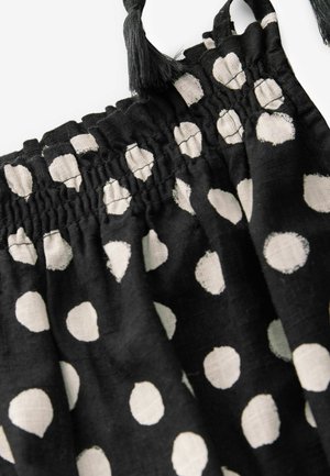 Schwarzer Stoff mit großen weißen Punkten, mit gerafftem elastischem Bund oben und dekorativen Quasten. Leicht und strukturiert.