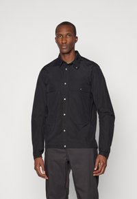Black lightweight jacket featuring snap-button closure, two front pockets, and a pointed collar. Smooth texture with a minimalistic design.