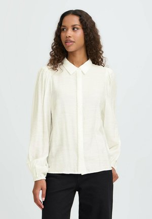 Blusa blanca de manga larga con botones en la parte delantera, cuello clásico y detalles fruncidos en los hombros; hecha de una tela ligera y texturizada.