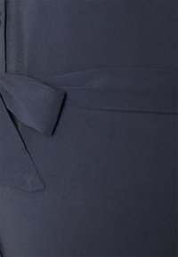 Tessuto blu scuro con una texture liscia presenta un dettaglio con sfilza legata. Il design è minimalista con un aspetto pulito ed elegante.