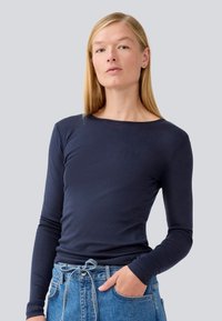 Camicia a maniche lunghe blu navy in morbido misto cotone con collo tondo. Presenta una silhouette aderente e una trama liscia, abbinata a jeans a vita alta blu.