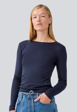 Navy long-sleeve shirt in soft cotton blend with a round neck. Features a fitted silhouette and smooth texture, paired with blue high-waisted jeans.