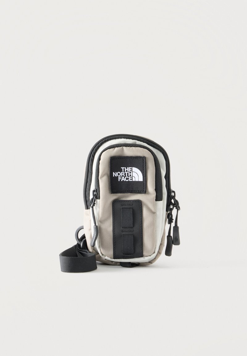 Μικρή τσάντα North Face μπεζ και μαύρο χρώμα με λογότυπο μπροστά, δύο θήκες με φερμουάρ και ρυθμιζόμενο λουρί ώμου.