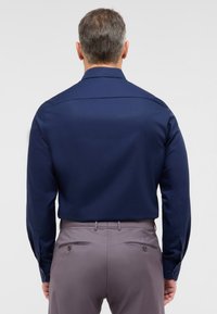 Donkerblauwe langemouwen shirt met een soepele textuur en subtiele glans, met een klassieke kraag en knoopmanchetten, gecombineerd met lichtgrijze broek.
